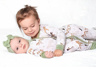 Boy holding baby girl both wearing bamboo zipper pajamas for babies and toddlers in Perfect Ponies print