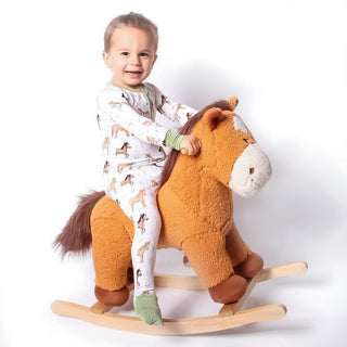 Boy wearing bamboo zipper pajamas for babies and toddlers in Perfect Ponies print smiling on a rocking horse