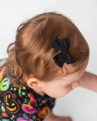 Girl wearing black bamboo clip on bow for babies and toddlers, and kids