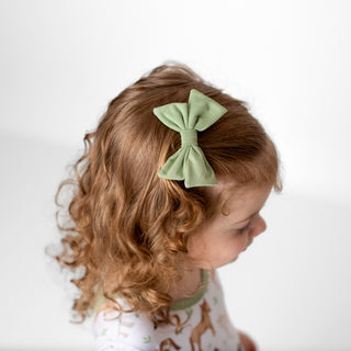 Girl wearing sage green clip on bow for toddlers and kids