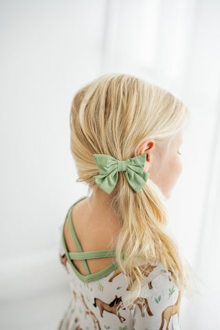 Girl wearing sage green clip on bow for toddlers and kids