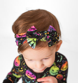 Girl wearing bamboo headband bow for babies, toddlers, and kids in Halloween Pumpkins print