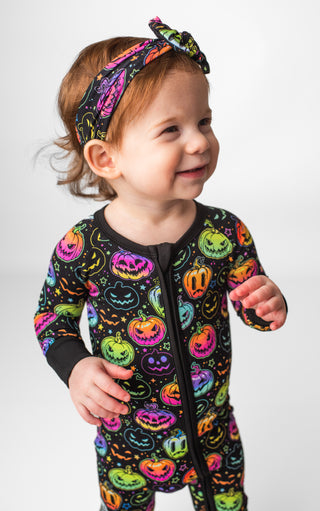 Girl wearing headband bow and bamboo zipper pajamas for babies and toddlers in Halloween Pumpkins print